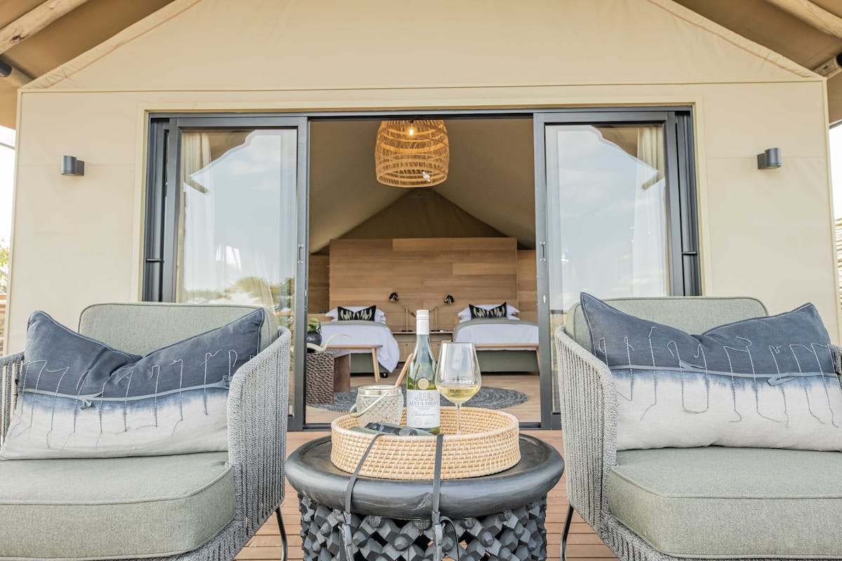 A cozy outdoor seating area with wicker chairs and a woven table centerpiece, leading to a private bedroom with a large bed and a hanging light fixture.