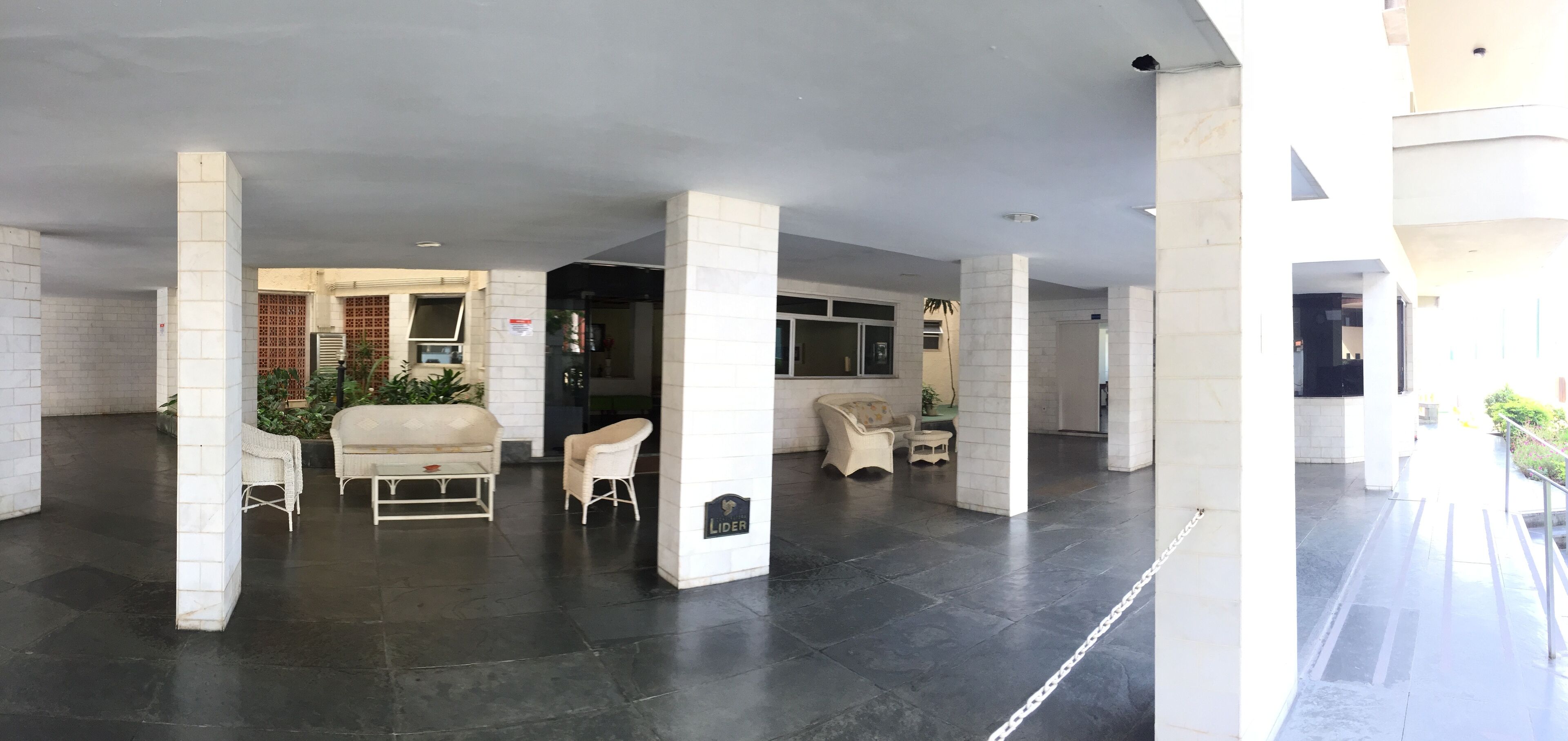 A spacious lobby with white pillars, dark tiled flooring, and several wicker chairs.
