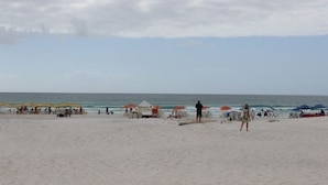 En strand med parasoller, strandstolar och några få personer.