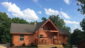 Une cabane en rondins avec un porche à l’avant, une cheminée et une petite terrasse.
