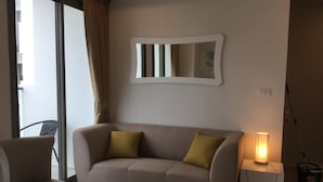 A modern living room with a sofa, a chair, a small table, a nightstand with a lamp, and a mirror on the wall. - Brand new resort close to beach at Pratumnak Hill (Pattaya City)