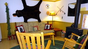 Un salon chaleureux avec un canapé, deux fauteuils à bascule, une cheminée, un sapin de Noël et une tête d’animal empaillée accrochée au mur.