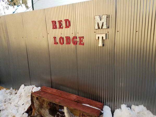 A corrugated metal wall with the text "RED LODGE" and a wooden bench partially covered in snow.