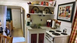 Une cuisine compacte équipée d’une cuisinière, d’un évier et d’un petit plan de travail. On aperçoit un coin repas avec une chaise et une table.