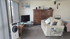 A living room with a sofa, a glass coffee table, a TV, a wooden cabinet, and a fan.
