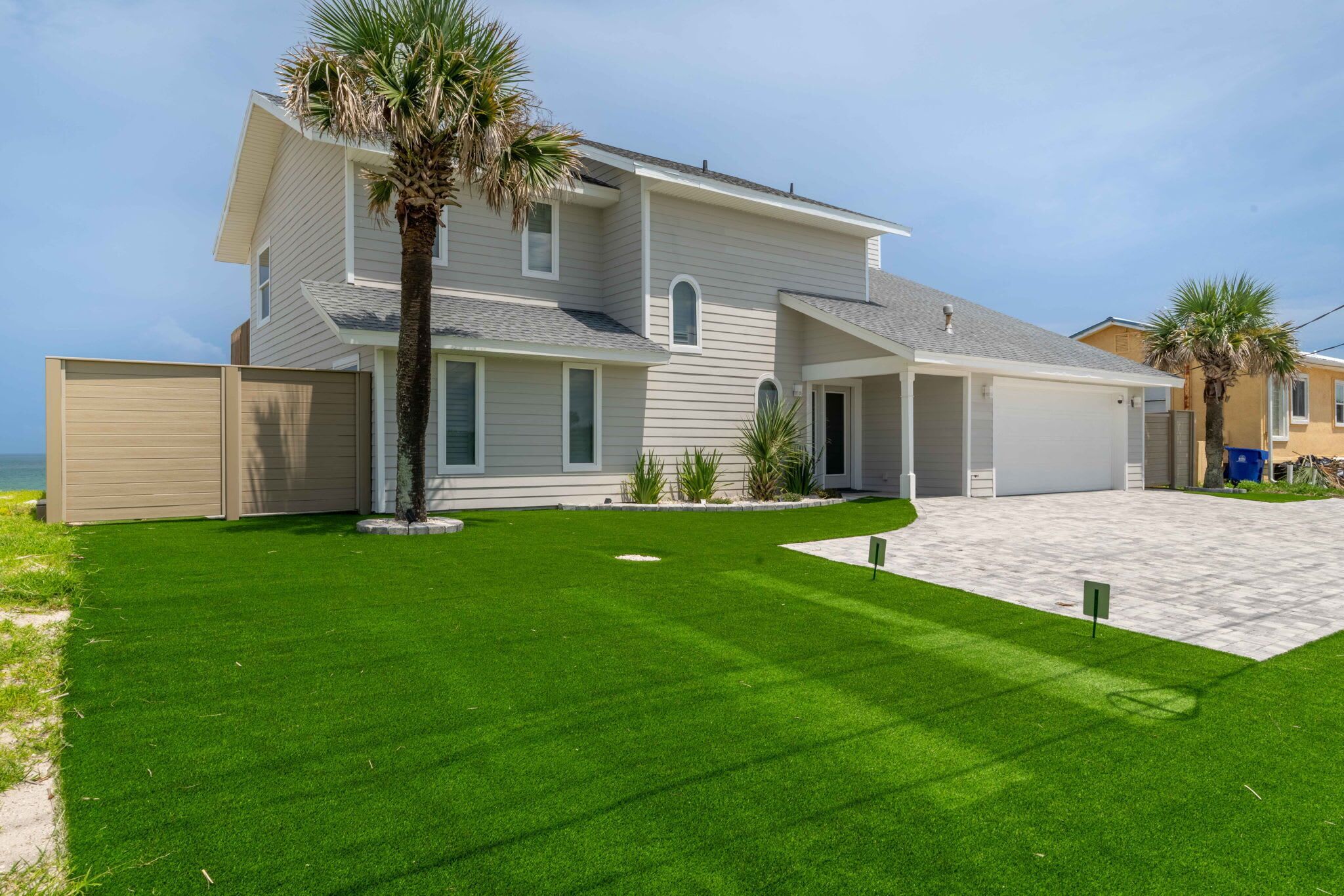 A two-story house with a covered garage, a well-maintained lawn, and a palm tree.