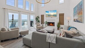 A spacious living room with a fireplace, comfortable seating, and a large window overlooking the ocean. - 4 BR Oceanfront | Large Deck, Handicap Friendly, Fire Pit & Putting Green! (Ponte Vedra Beach)
