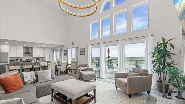 A spacious living area with a large sofa, a coffee table, and a view of the ocean through large windows. - 4 BR Oceanfront | Large Deck, Handicap Friendly, Fire Pit & Putting Green! (Ponte Vedra Beach)