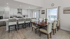 A modern kitchen with white cabinets, a wooden dining table, and a view of the ocean through large windows. - 4 BR Oceanfront | Large Deck, Handicap Friendly, Fire Pit & Putting Green! (Ponte Vedra Beach)