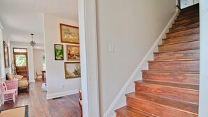 Un escalier en bois menant à un deuxième étage, un couloir avec un plancher en bois et un coin repas avec des meubles en osier.