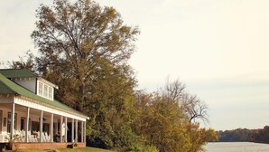 Une maison à deux étages, dotée d’un porche et d’un toit végétalisé, entourée d’arbres et bordée par un plan d’eau.