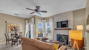 A living room with a sofa, dining table, chairs, a fireplace, a TV mounted on a brick wall, and a ceiling fan. - Immaculate PC condo - Extended Stay or Monthly rental, KING BED,  carport, W/D (Park City)