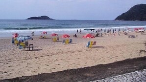A beach with umbrellas and chairs, a sandy shore, and a view of the sea and a distant island. - Guarujá-Enseada - 1 Bedroom Apartment with Pool (Guarujá)
