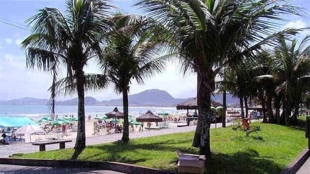 A beachside resort with palm trees, a pool, and beach umbrellas. - Guarujá-Enseada - 1 Bedroom Apartment with Pool (Guarujá)
