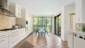 Una cocina moderna con armarios blancos, un salpicadero de piedra y un comedor con mesa y sillas de vidrio.