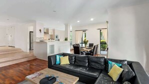 Una sala moderna con un sofá de cuero negro, una mesa de centro de madera y un área de comedor al fondo.