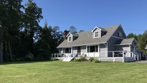Uma casa de dois andares com varanda, chaminé e gramado bem cuidado.