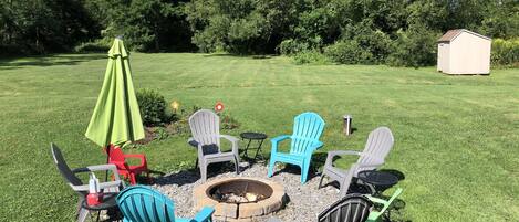 Ein Garten mit einem Feuerkorb, umgeben von Gartenmöbeln, darunter Stühle und ein Tisch.