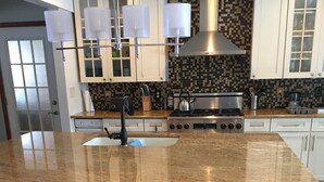 Uma cozinha com bancada de granito, eletrodomésticos de aço inoxidável e armários brancos.