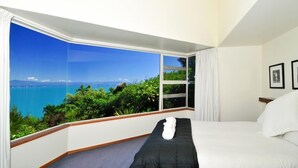 A bedroom with a large window offering a view of the sea and greenery.