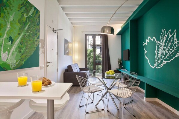 A modern living space with a dining area, a sofa, and a green accent wall.