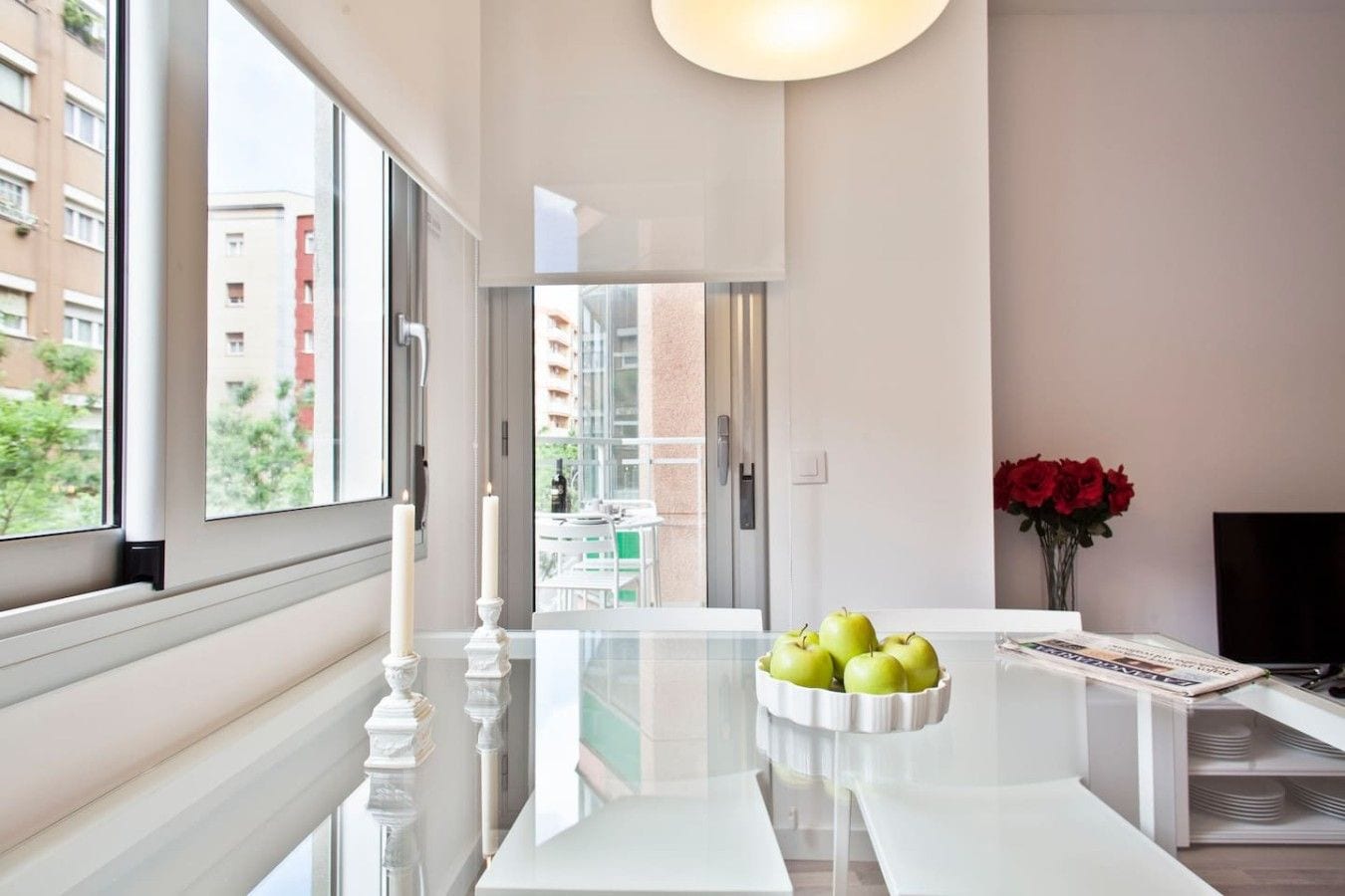 A modern kitchen with a white countertop, a bowl of green apples, and a vase of red flowers.