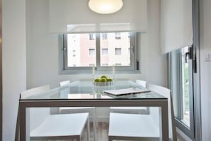 A modern dining area with a glass table and white chairs, a candle, and a bowl of green apples.