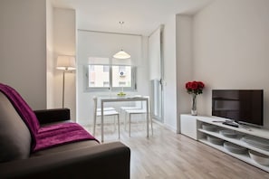 A modern living room with a sofa, a dining table with chairs, a TV, and a vase with flowers.