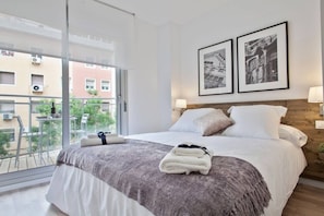 A hotel room with a large bed, a balcony with a view of buildings, and two framed pictures on the wall.