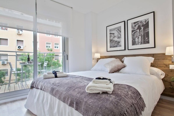 A hotel room with a large bed, a balcony with a view of buildings, and two framed pictures on the wall.