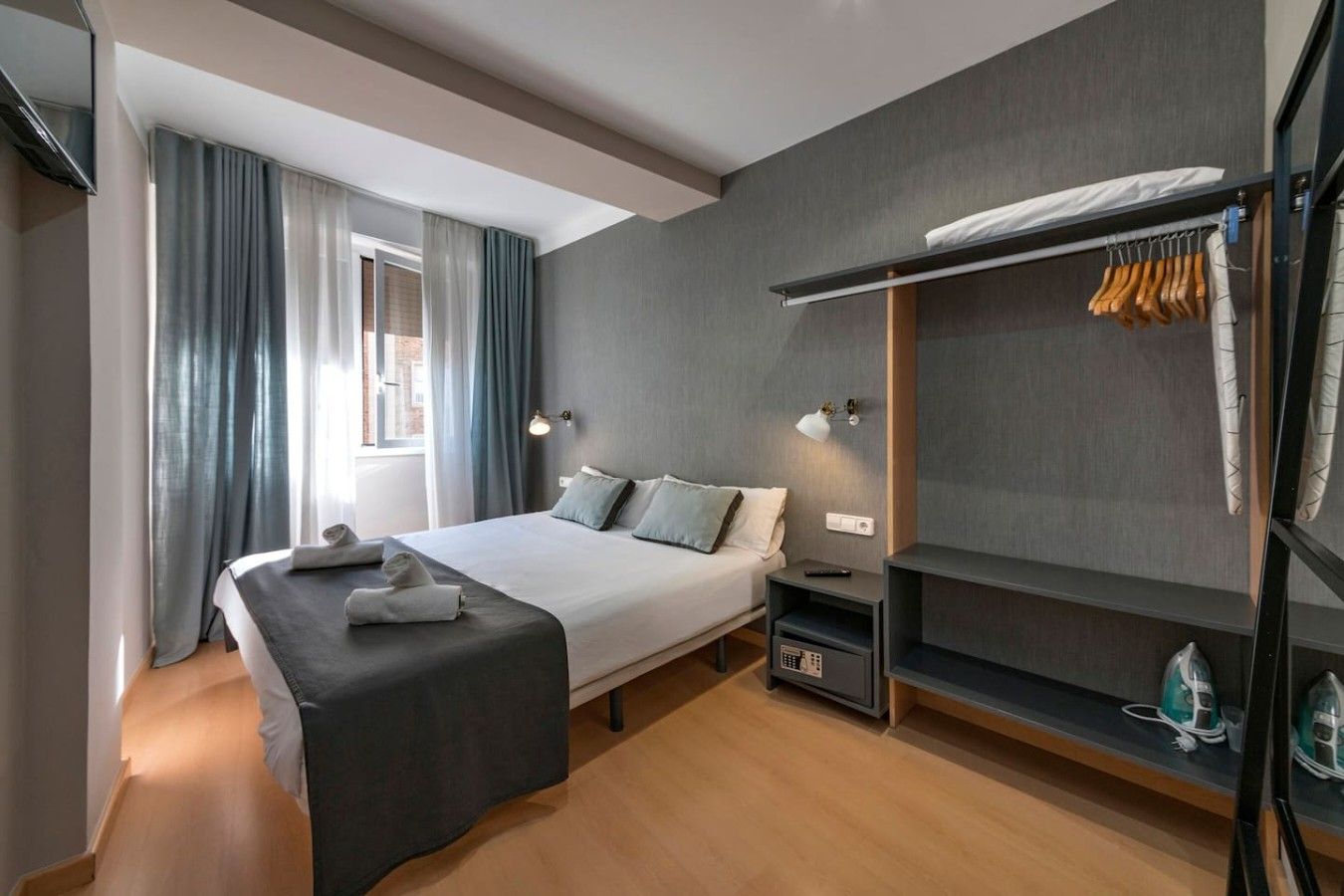 A modern hotel room with a bed, bedside tables, a wardrobe, and a window with curtains.
