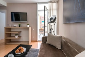 A modern living room with a flat-screen TV, a sofa, a coffee table with croissants, and a floor lamp. - Cool Jazz 44 - Habitat Apartments (Barcelona)