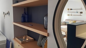 Quarto moderno com estante embutida, uma pequena mesa com uma vela e um espelho refletindo uma cama e objetos decorativos fixados na parede.