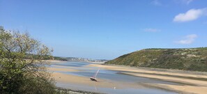 A coastal landscape with a sandy beach, a small boat, and a hill with sparse vegetation. - Waterside Cottage Wadebridge River views Camel Trail Cycling Free Wi-Fi Cornwall (Wadebridge)