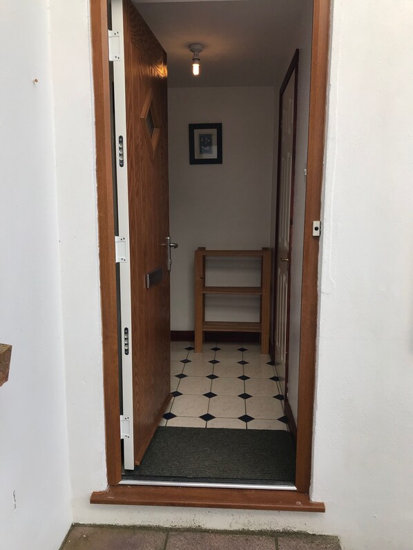 A narrow hallway with a wooden door, a tiled floor, a small wooden bench, and a framed picture on the wall. - Waterside Cottage Wadebridge River views Camel Trail Cycling Free Wi-Fi Cornwall (Wadebridge)