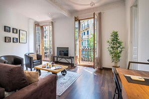 A living room with a sofa, a coffee table, a TV, and a balcony with a view of buildings. - Barcelona Balconies 10 - Habitat Apartments (Barcelona)