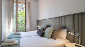 Une chambre d’hôtel avec deux lits, une table de chevet avec une lampe et une vue sur un balcon agrémenté de verdure.