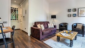 Un salon avec un canapé violet, deux fauteuils noirs, une table basse en bois et un lampadaire.