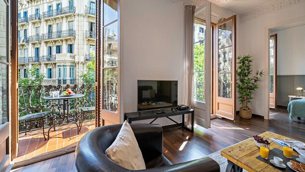 Un salon moderne doté d’un grand téléviseur, de meubles en bois et d’un balcon offrant une vue sur un bâtiment historique.