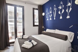 Habitación de hotel con cama, cortinas, vista al balcón e ilustraciones de peces en la pared.