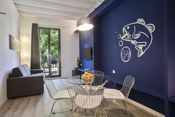 Un salon moderne avec une table à manger en verre, des chaises en métal, un canapé et une grande fresque représentant des poissons sur le mur.