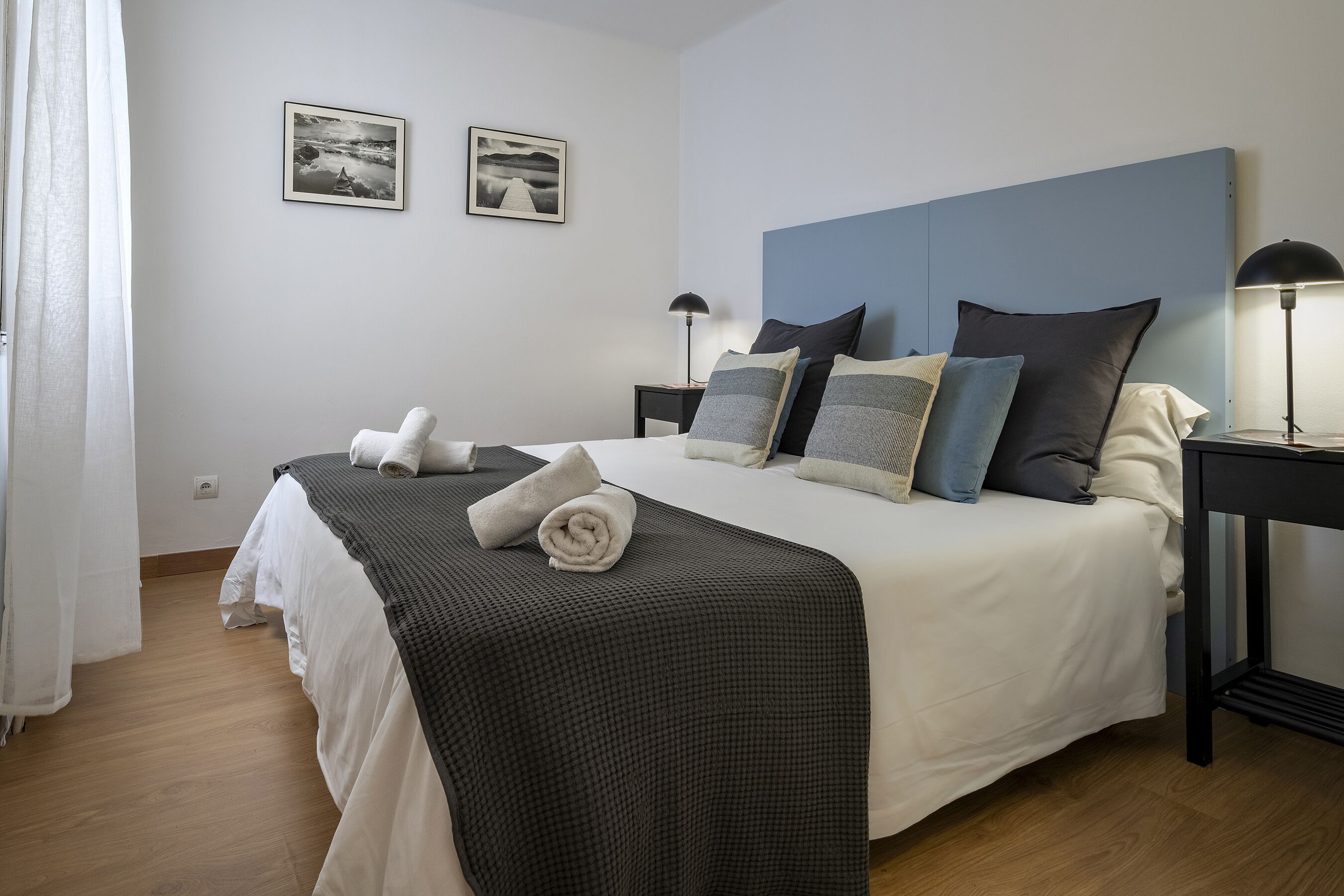 A neatly made bed with a checkered blanket, two bedside lamps, and two framed pictures on the wall.