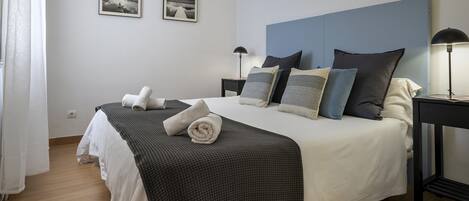 A neatly made bed with a checkered blanket, two bedside lamps, and two framed pictures on the wall.