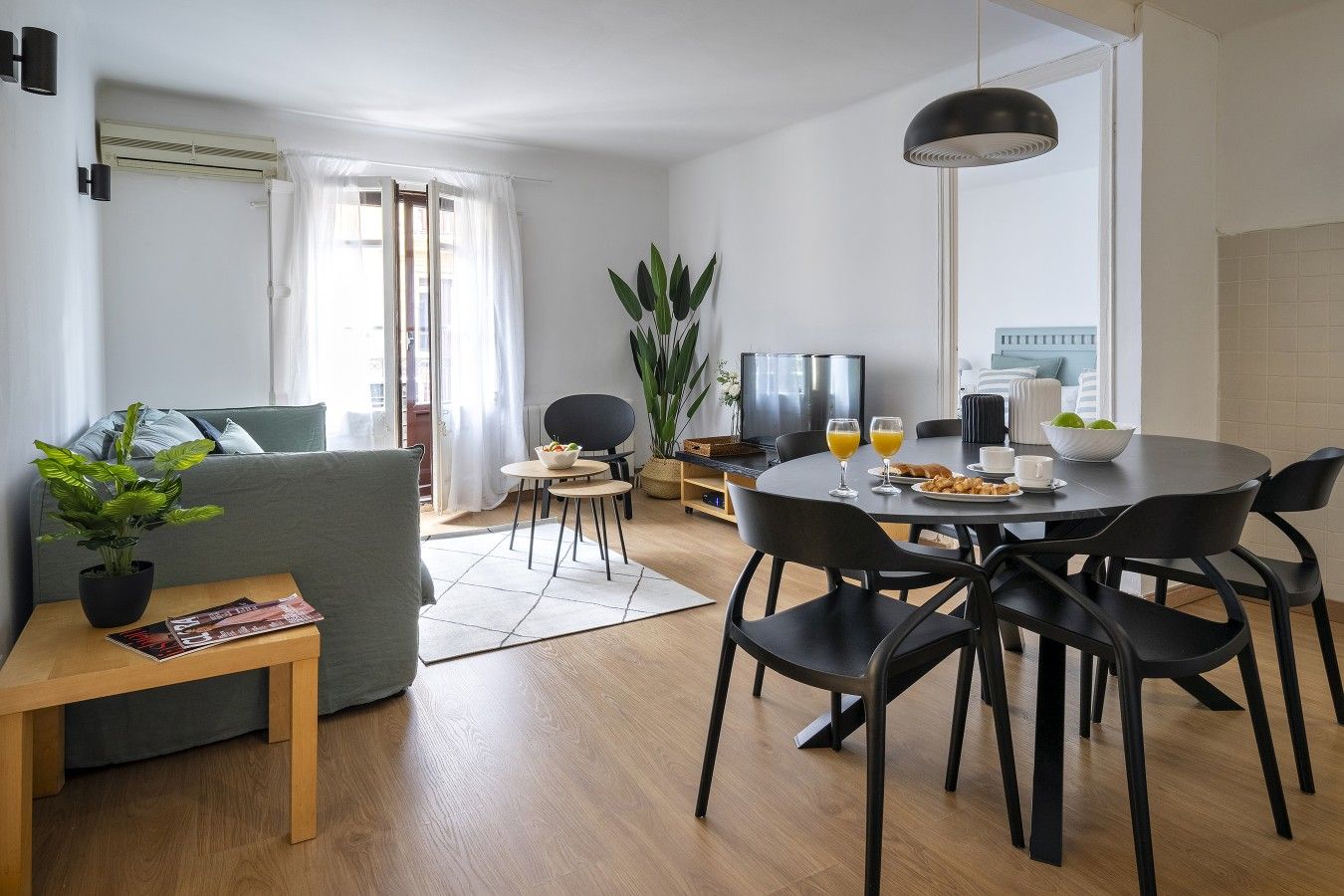 A modern living room with a sofa, coffee table, and a dining area with chairs and a table set for breakfast.