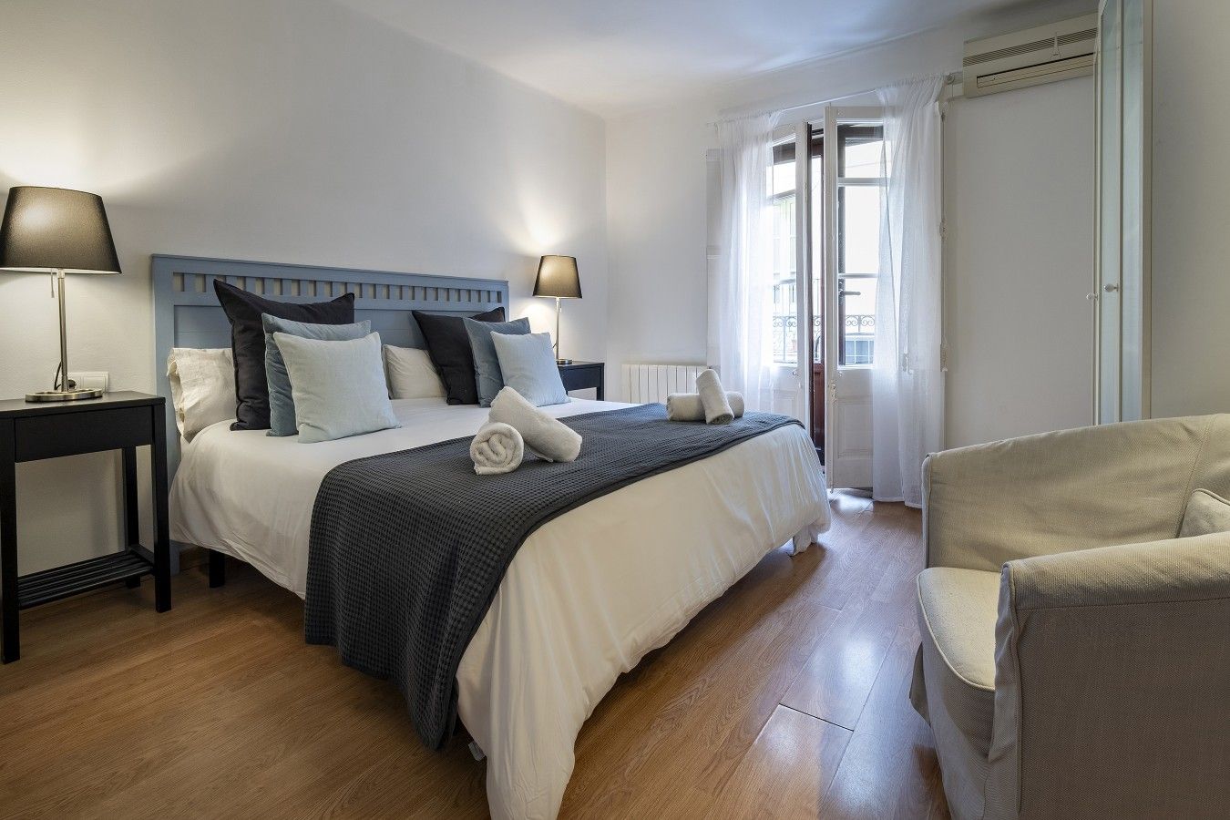 A hotel room with a bed, two bedside tables, a chair, and a window with curtains.