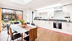 A modern kitchen with white cabinets, a dining area with a table and chairs, and a view of a garden through large windows. - Modern, Chic 3BR Townhouse in Central Oxford - Pass the Keys (Oxford)