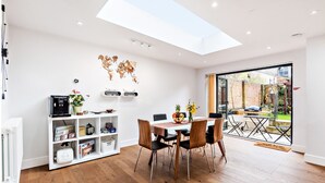 A modern dining area with a wooden floor, a white table, and chairs. There is a white shelving unit with various items and a world map on the wall. - Modern, Chic 3BR Townhouse in Central Oxford - Pass the Keys (Oxford)