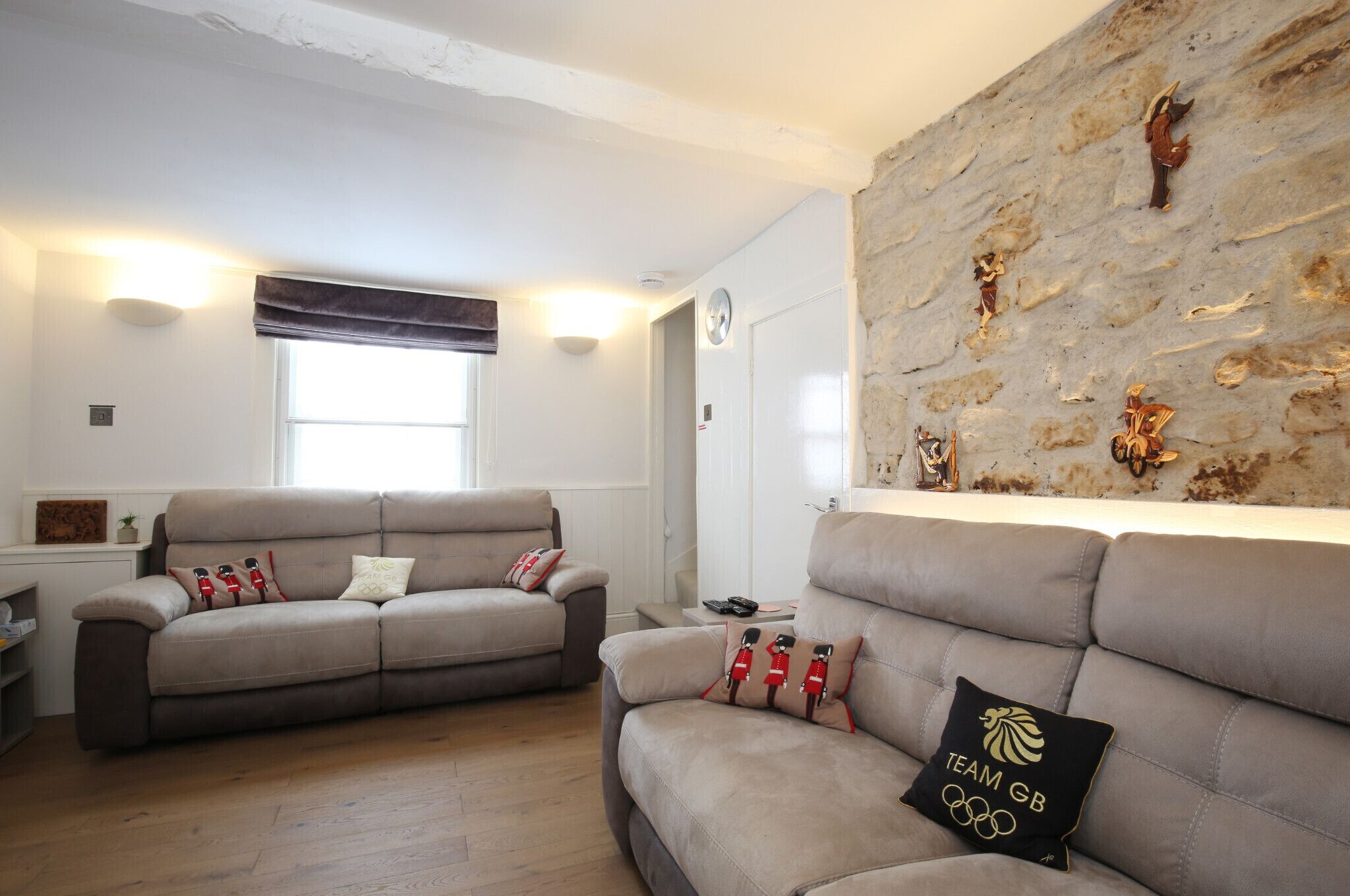 A living room with two sofas, a stone wall with decorative items, and a window with blinds.