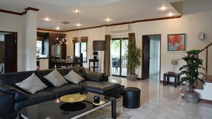 Un salón amplio con un sofá de cuero negro moderno, una mesita de centro y un comedor con candelabro.