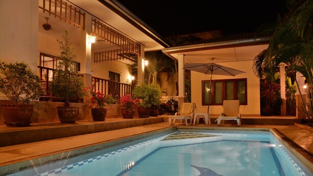 Piscina con diseño de delfines en azulejos, rodeada de plantas en macetas y mobiliario de exterior.